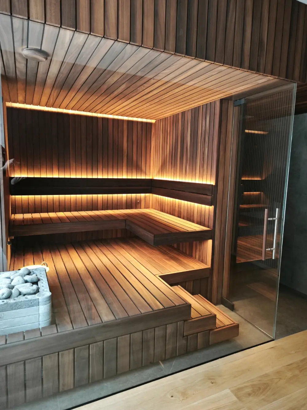 Thermo Abachi cladding and benches in a sauna interior with a glass door.